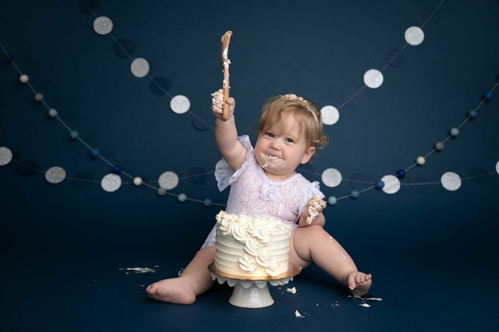 1 year old baby in a studio ready to smash a cake in front of them with wooden spoon.