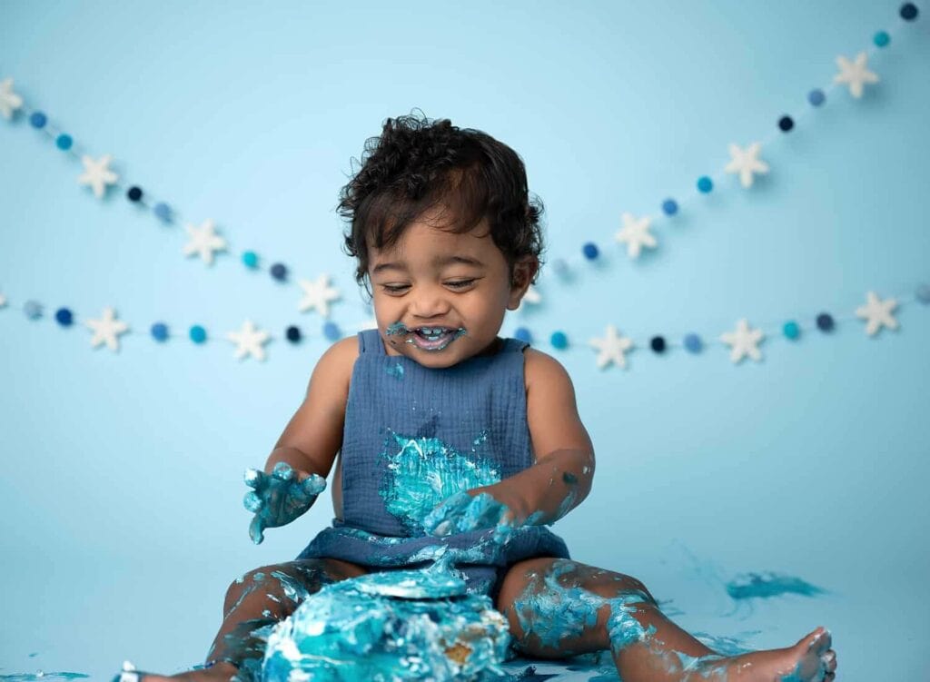 A 1 year old boy smashing a blue cake. All details and accessories are blue.