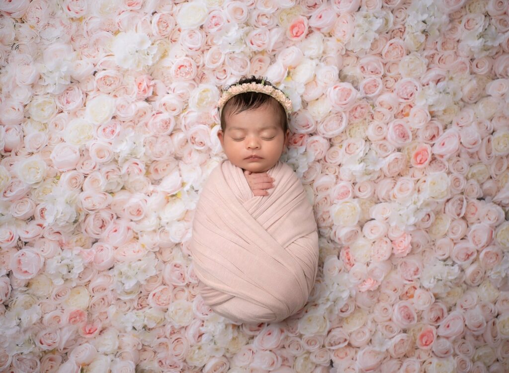 Newborn baby wrapped in pink, laying on a bed of pink and white flowers.